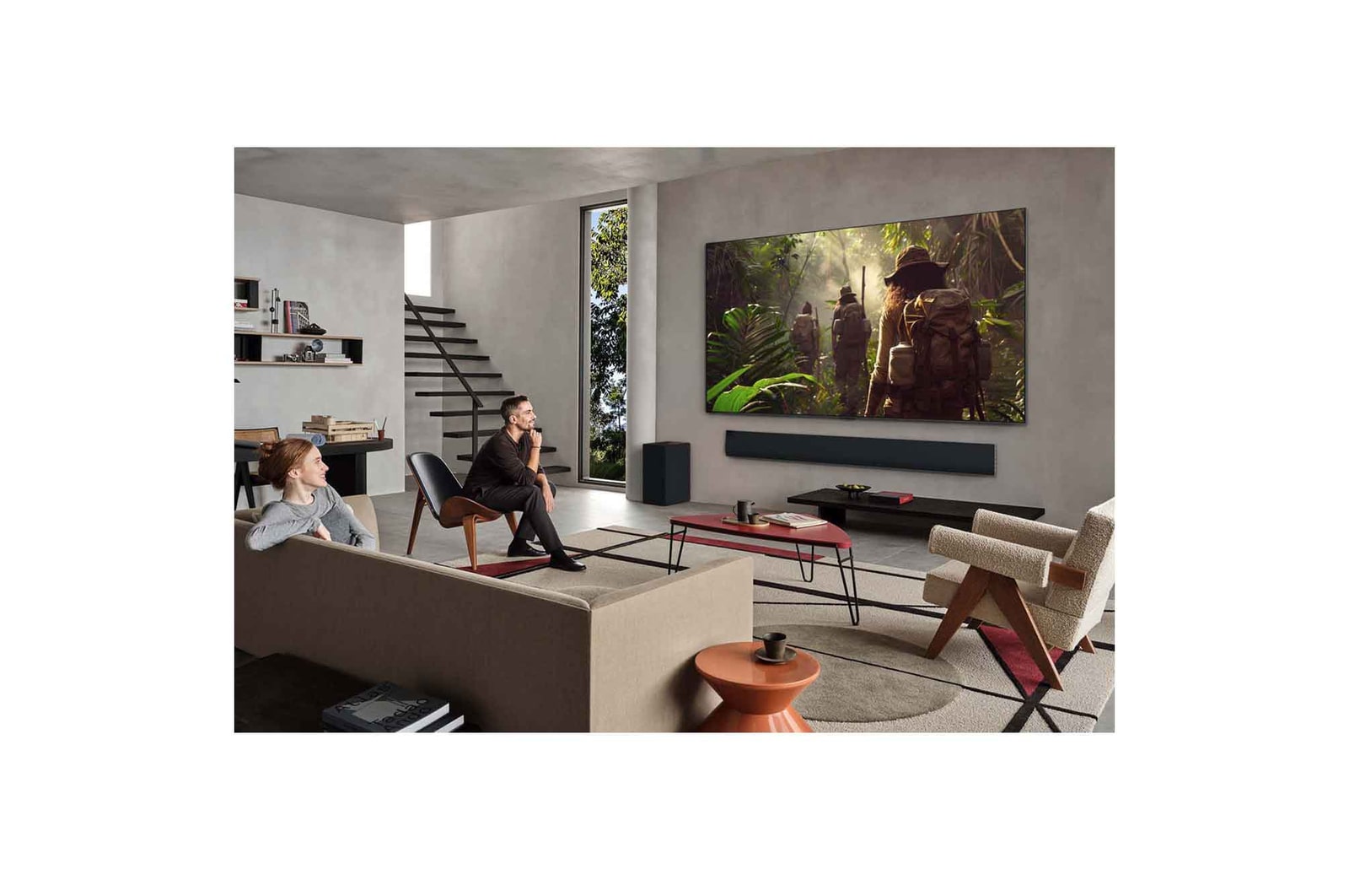 Wide view of a living room inside a premium home, a man is watching a movie on his wall-mounted LG OLED TV. The TV's design blends elegantly with the wall and the interior design.