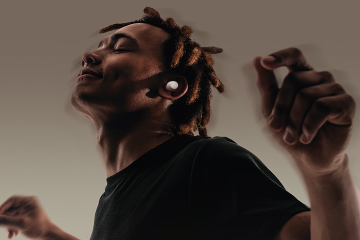 Ein Mann, der xboom Buds Plus im Ohr trägt, bewegt sich mit beiden Armen, als würde er tanzen. Das Spektrum von ihm deutet darauf hin, dass die Adaptive EQ-Funktion funktioniert, während sich der Benutzer bewegt.