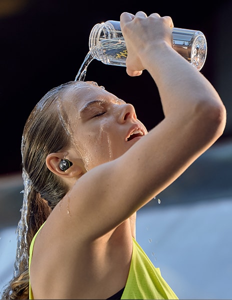 Eine Frau gießt sich Wasser ins Gesicht und hat DTF7Q am Ohr.