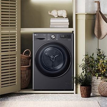 LG Trockner RT90V9B in Dunkelschwarz, elegant in einen hellgrünen Waschraum mit Holzakzenten und Pflanzen integriert.