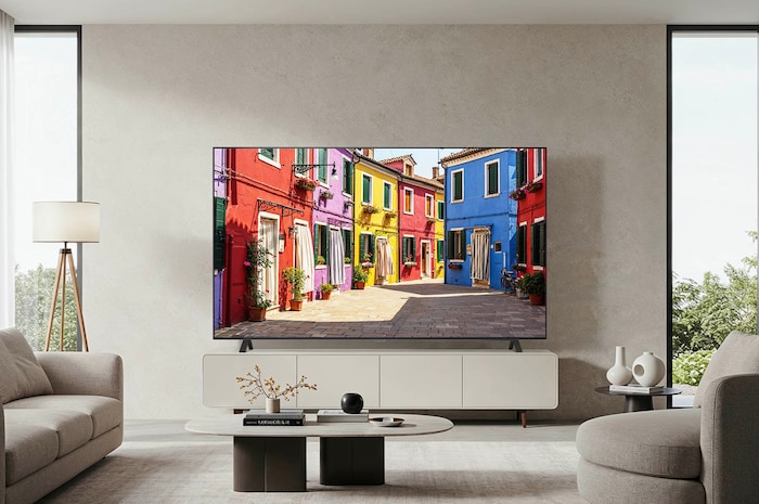 Lifestyle-Aufnahme des LG OLED AI B4 4K Smart TV auf seinem Standfuß in einem modernen Wohnzimmer, das eine bunte Straßenszene zeigt.