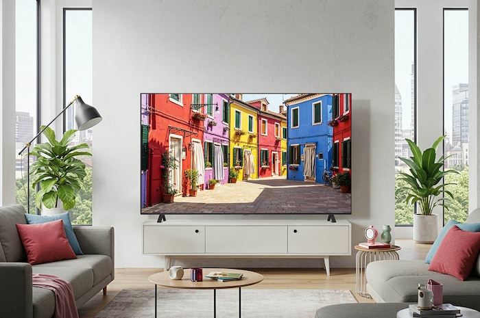 Lifestyle-Aufnahme des LG OLED AI B4 4K Smart TV auf seinem Standfuß in einem modernen Wohnzimmer, das eine bunte Straßenszene zeigt.