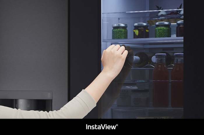 LG Side-by-Side GSXV90MCAE zeigt **InstaView** Door-in-Door: Eine Hand greift nach einer Flasche durch die halb geöffnete Innentür, wobei das beleuchtete Fach sichtbar ist.