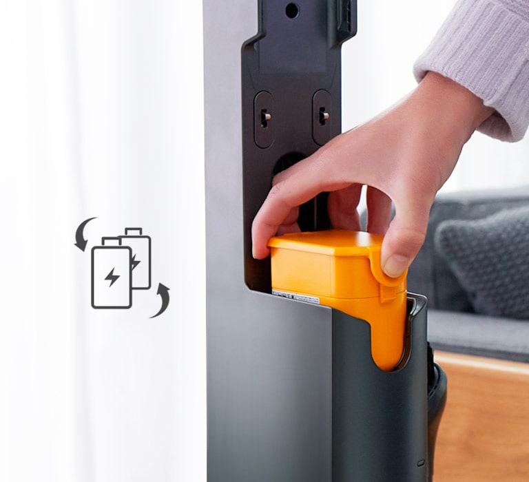 Eine Hand setzt den Akku in den Staubsauger ein. Auf der linken Seite befindet sich ein Symbol mit zwei Akkus mit  60 Minuten und Pfeilen an der Seite. Die Batterien bewegen sich, um anzuzeigen, dass sie ausgetauscht werden können.