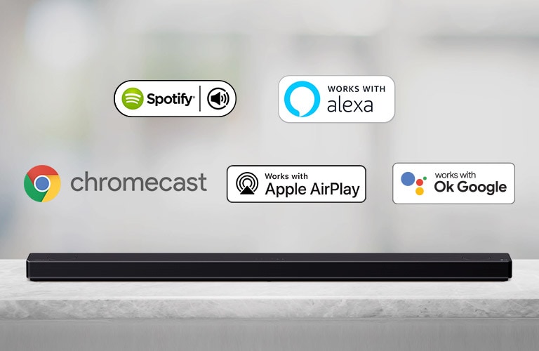 Auf einem grauen Regal steht eine Soundbar, auf der von links nach rechts die Logos von AI-Plattformen in der folgenden Reihenfolge zu sehen sind: Spotify, Alexa, Chromecast, Apple Airplay und OK Google.