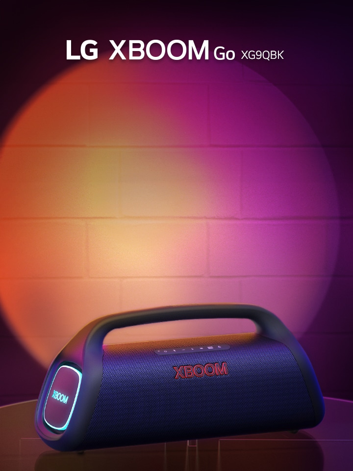 Das LG XBOOM Go DXG9Q steht auf einem Metalltisch und ist orange beleuchtet. Hinter dem Tisch strahlt die Bühnenbeleuchtung die Wand an.
