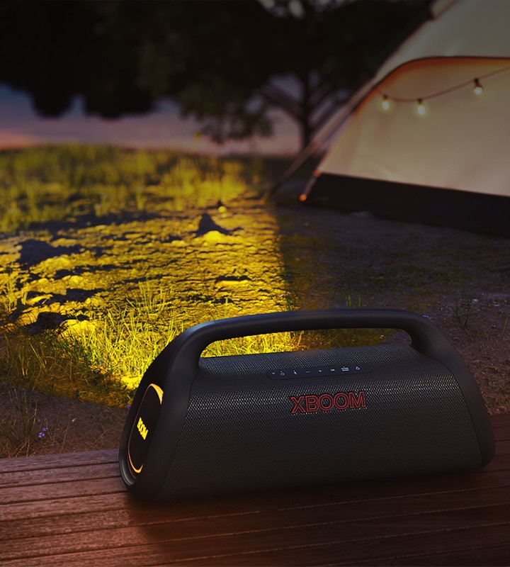 LG XBOOM Go wird auf dem Holzdeck platziert. Es wirft ein Bühnenlicht auf den Campingplatz.