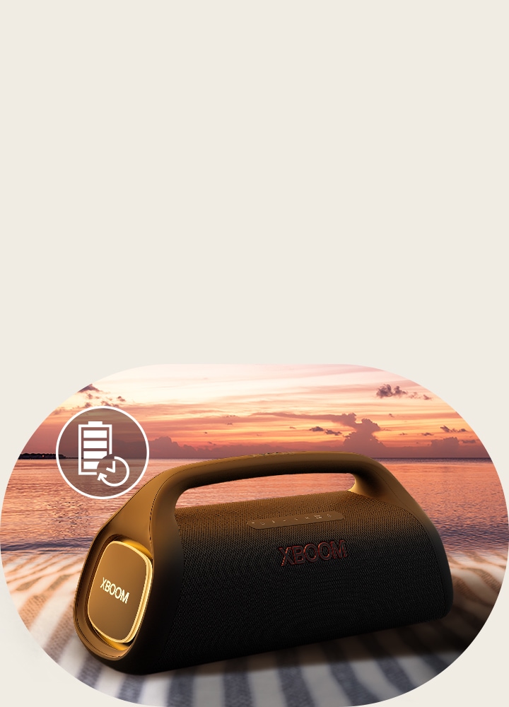 Der Lautsprecher wird auf ein Strandtuch gestellt. Vor dem Lautsprecher ist ein Sonnenuntergang am Strand abgebildet, um zu verdeutlichen, dass dieser Lautsprecher länger betrieben werden kann.