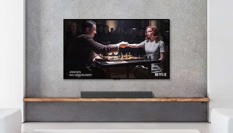 Eine Soundbar und ein Fernseher befinden sich in einem weiß eingerichteten Wohnzimmer. Im Fernsehen spielen eine Frau und ein Mann Schach.