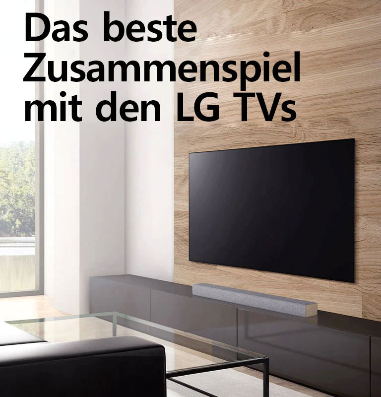 Eine Soundbar steht auf einem weißen TV-Schrank und der Fernseher hängt an einer holzvertäfelten Wand. Draußen sind Bäume zu sehen. Text erscheint auf dem Bild: Das beste Zusammenspiel mit den LG TVs.