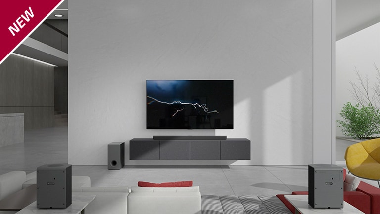 Eine Sound Bar steht in einem Wohnzimmer auf einem grauen TV-Regal unter einem wandmontierten Fernseher. Ein kabelloser Subwoofer steht links davon auf dem Boden und die Sonne scheint von rechts in den Raum. Ein langes Sofa in Rot und Weiß steht gegenüber dem Fernsehgerät und der Sound Bar. In der linken oberen Ecke steht „NEU“.