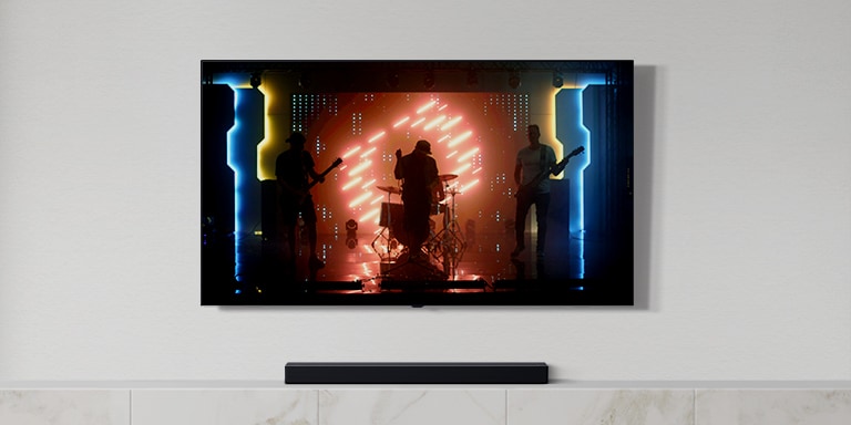 In einem hellen Wohnzimmer stehen ein TV und eine Soundbar. Auf dem TV-Bildschirm ist eine Musikband zu sehen (Video abspielen).