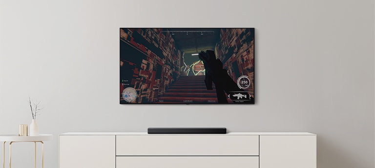 In einem Wohnzimmer befinden sich ein TV und eine Soundbar. Auf dem TV-Bildschirm läuft ein FPS-Spiel und der TV-Kanal ist auf Fußballspiel eingestellt (Video abspielen).