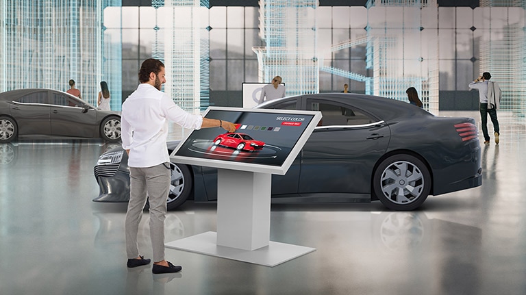 In a car dealership, a man is touching TNF5J to change the color of a car on the display.