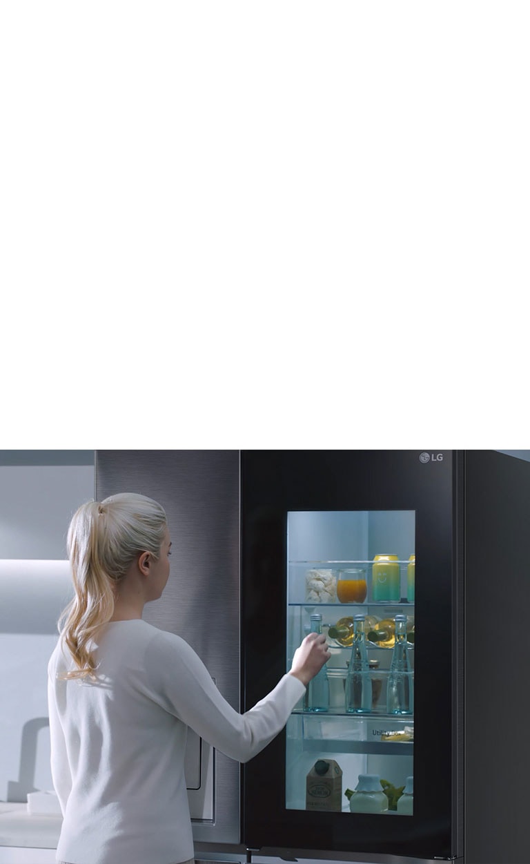 Ein Video zeigt eine Frau, die sich ihrem InstaView-Kühlschrank nähert und zweimal anklopft. Der Innenraum leuchtet auf, und sie kann den Inhalt ihres Kühlschranks sehen, ohne die Tür öffnen zu müssen. Die Ansicht zoomt heran, sodass die Getränke in der Tür zu sehen sind, und zoomt dann heraus, um die Frau von hinten zu zeigen, wie sie die Tür öffnet und sich ein Getränk nimmt.