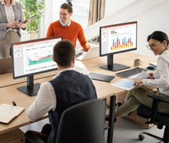 Employees sitting at office desks and having a conversation.	