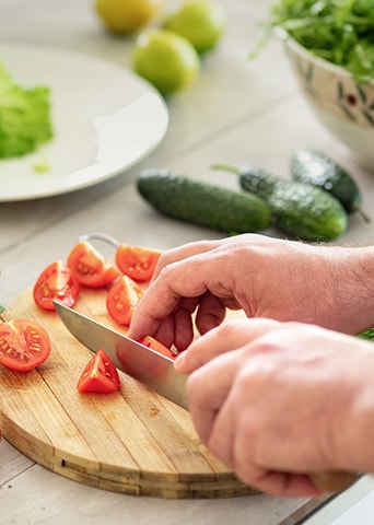 Bild vom Schneiden von Tomaten auf einem Schneidebrett mit einem Messer.