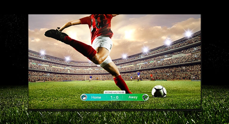Ein Bild des Displays zeigt ein Fußballspiel mit einem Spieler in einem roten Trikot, der den Ball quer durch das Stadion schießt. Der Spielstand ist am unteren Rand des Bildschirms zu sehen. Das grüne Gras des Spielfelds erstreckt sich über den Bildschirm hinaus bis zum schwarzen Hintergrund.