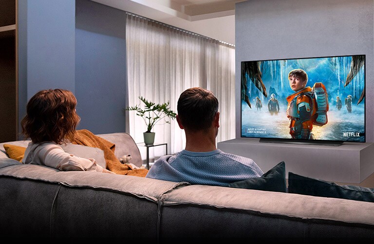 Ein Paar sitzt auf der Wohnzimmercouch und sieht sich einen romantischen Film an.