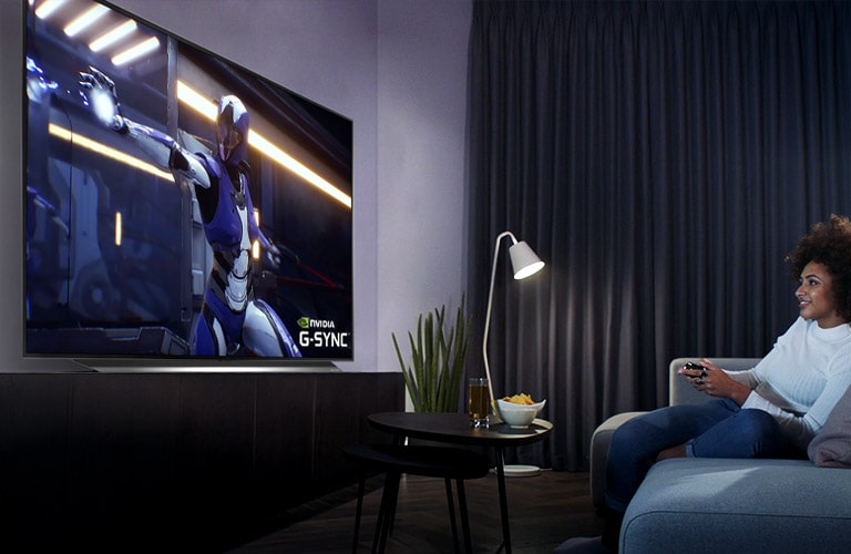 Eine Frau, die auf einem Sofa sitzt und einen Controller hält, während sie ein Spiel auf dem Fernseher spielt