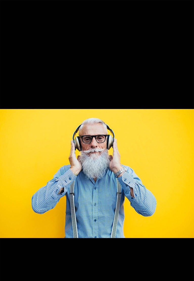 Ein älterer Mann steht vor einer gelben Wand und trägt ein Headset.