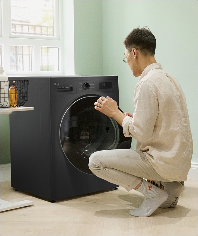 Mann lädt Kleidung in eine Waschmaschine, während die Einstellungen eingestellt.