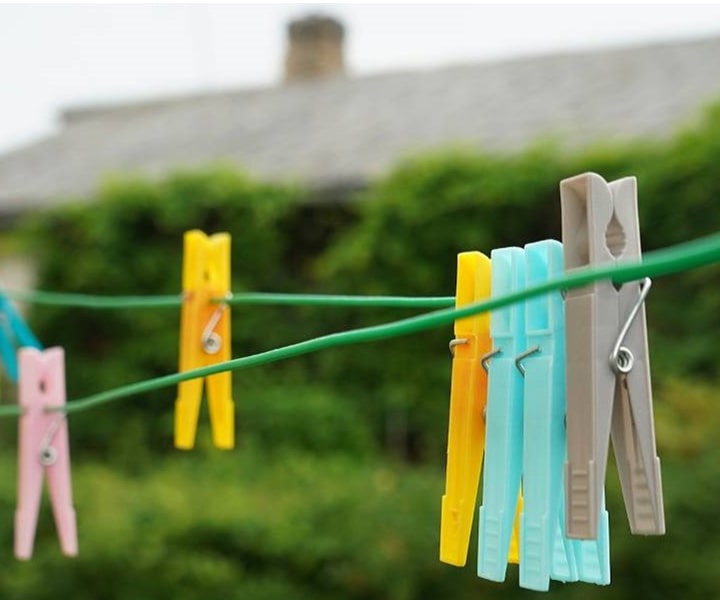 Bild von gelben, blauen, grauen, rosafarbenen Wäscheklammern auf dem Draht im Freien.