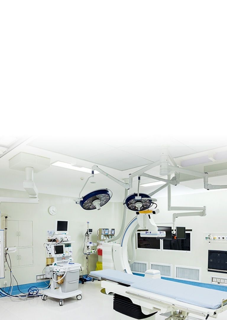 En operationsstue med hvide vægge og patientens seng, flere medicinske enheder forbundet via elektriske kabler og monitorer med sort skærm.