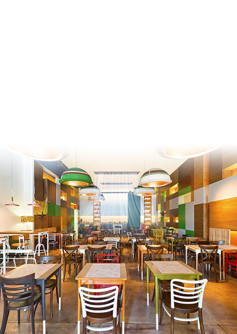 Loftsmonterede enheder laver blå luftstrømme i et cafeteria med rækker af stole og borde. Der hænger en rund lampe fra loftet over hvert sæde.