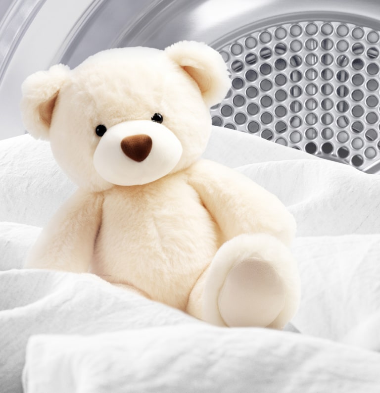 Billede af en ren bamse og hvidt stof inde i en tørretumbler.