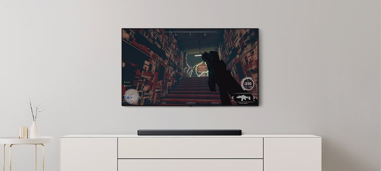 Der er et tv og en soundbar i en stue. Et FPS-spil vises på en tv-skærm, og tv-kanalen skiftes til en fodboldkamp. (afspil videoen)