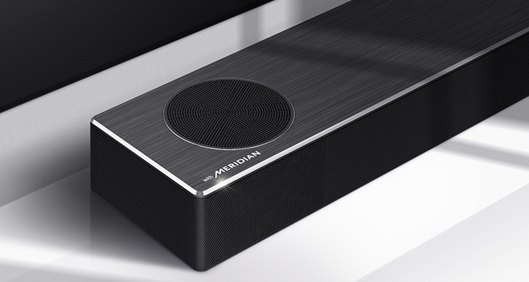 Nærbillede af venstre side af en LG Soundbar med et Meridian-logo vist nederst i venstre hjørne på et produkt. Nederste venstre side af tv’et er også synligt.