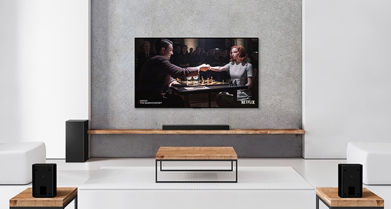 Et sæt med to baghøjtalere, en subwoofer, en soundbar og et tv i en hvid stue En plakat med en tv-serie vises på tv-skærmen.