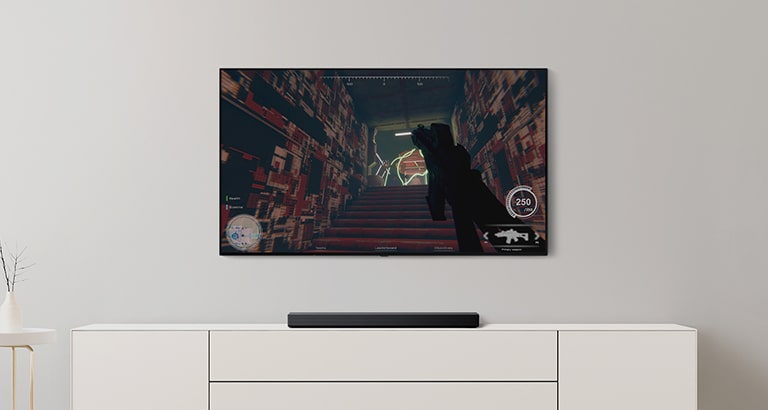 Der er et tv og en soundbar i en stue. Et FPS-spil vises på en tv-skærm, og tv-kanalen skiftes til en fodboldkamp. (afspil videoen)