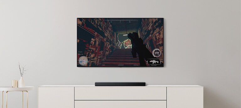 Der er et tv og en soundbar i en stue. Et FPS-spil vises på en tv-skærm, og tv-kanalen skiftes til en fodboldkamp. (afspil videoen)
