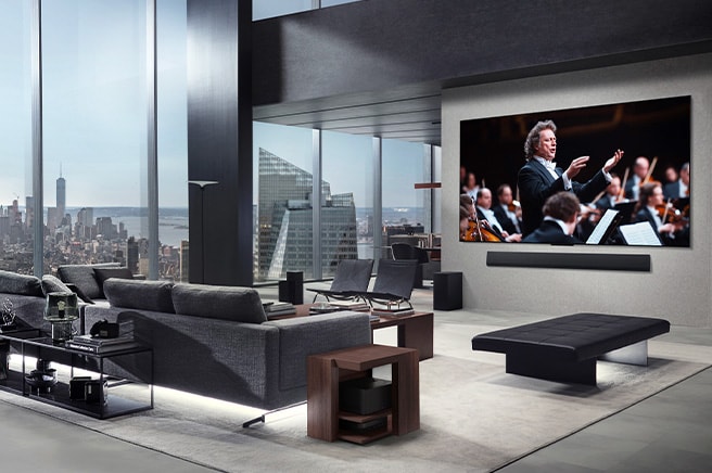 Stue med et LG True Wireless TV og en LG Soundbar, som er vægmonteret. Zero Connect Box kan knap ses under et sidebord ved sofaen, hvilket demonstrerer, hvordan den kan placeres hvor som helst. Hele stuens indretning er visuelt pæn og ryddelig. 