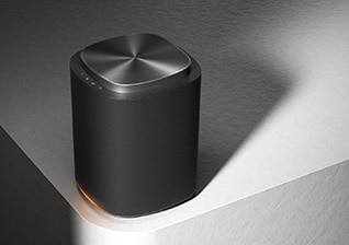 LG Sound Suite-højttaler på en bordplade med en afrundet mørk form og en blød orange glød ved basen.
