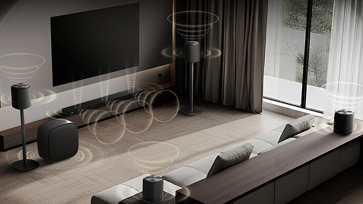 LG TV med Sound Suite er vægmonteret i en moderne stue, med flere højttalere arrangeret omkring en sofa, mens visualiserede lydbølger stråler udad, hvilket illustrerer en fleksibel lydopsætning skræddersyet til rummet.