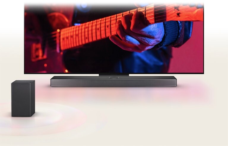 LG TV يعرض رجلاً يعزف على الجيتار وLG Soundbar أسفله مباشرة، مع وجود مكبر صوت آخر في الأمام.