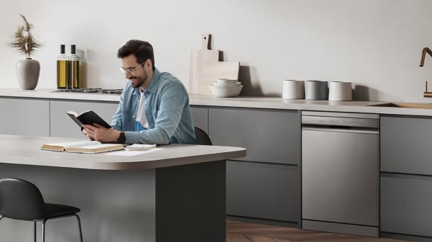 LG silver Freestanding Dishwasher integrated into a modern gray kitchen beside a dining island and countertop workspace.