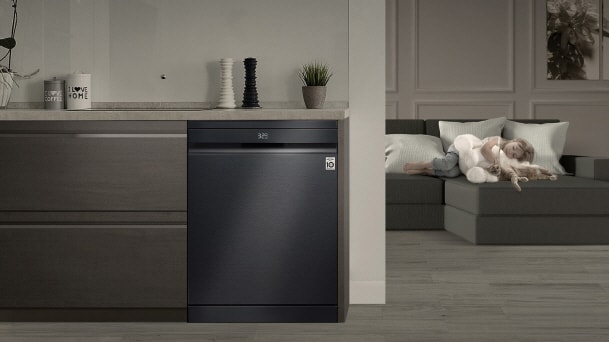 LG Matte Black Dishwasher installed in a chic urban studio kitchen beside a living room with sofa and child.
