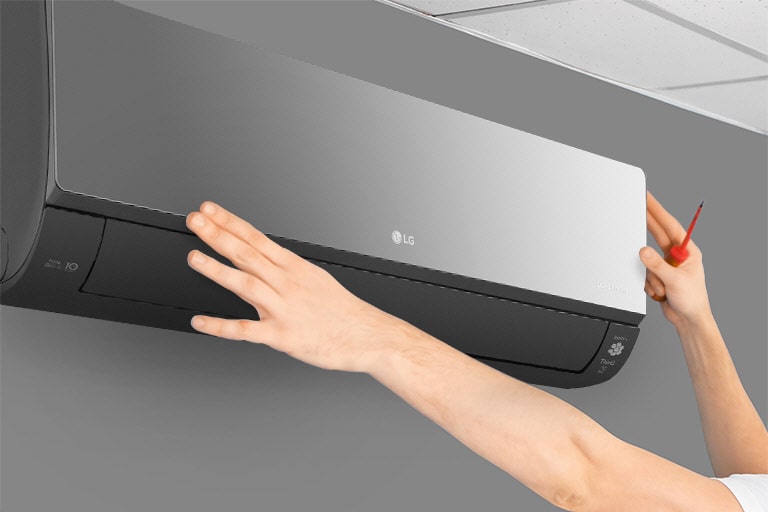 Hands adjusting an LG wall-mounted air conditioner on a gray wall, with a ceiling panel in the background.