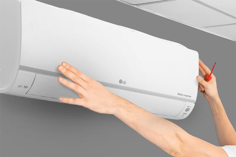 Technician carefully aligns and secures an LG Dual Inverter air conditioner on a gray wall, ensuring proper installation.