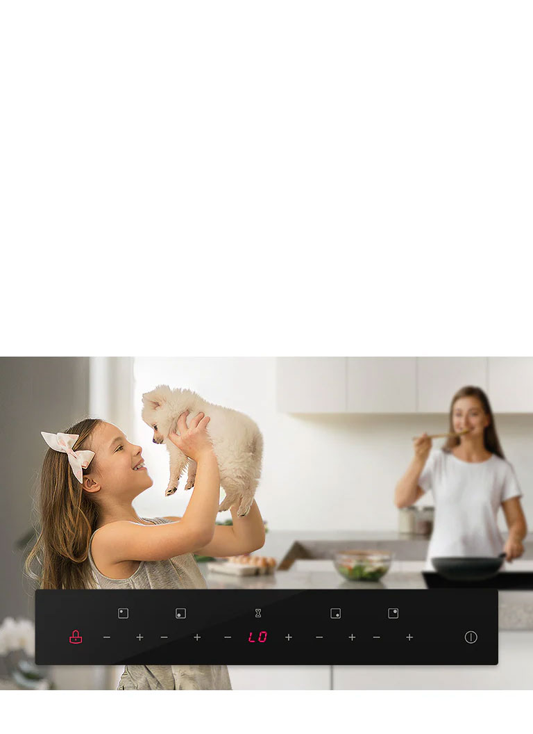 Woman lifting a puppy in a modern kitchen with digital stove controls in the foreground and another woman cooking.