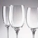 Three clear wine glasses of different sizes are arranged in a row against a neutral background.