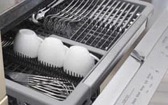  Dishwasher rack fully extended with clean cutlery and three white bowls placed upright, ready for unloading.