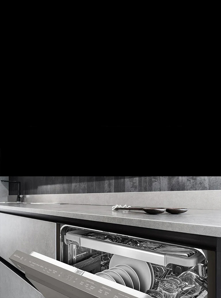  LG dishwasher open on a sleek countertop with dishes inside, grey utensils on the counter, and dark wall tiles.