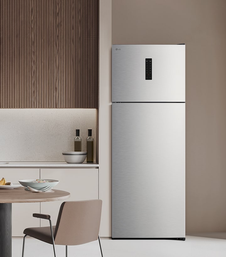 Top freezer refrigerator placed in a modern kitchen with wooden wall panels and a clean table setting