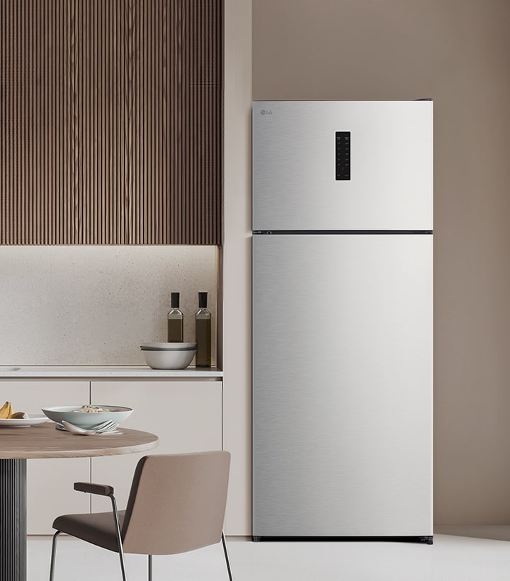 Top freezer refrigerator placed in a modern kitchen with wooden wall panels and a clean table setting