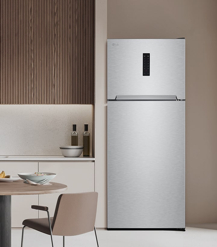 Top freezer refrigerator placed in a modern kitchen with wooden wall panels and a clean table setting